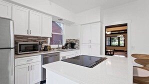 A modern kitchen with white cabinets, a built-in microwave, and a large island with a black countertop. - Quaint South Hill Home w/ Luxury King Bed & Wifi! (Spokane)