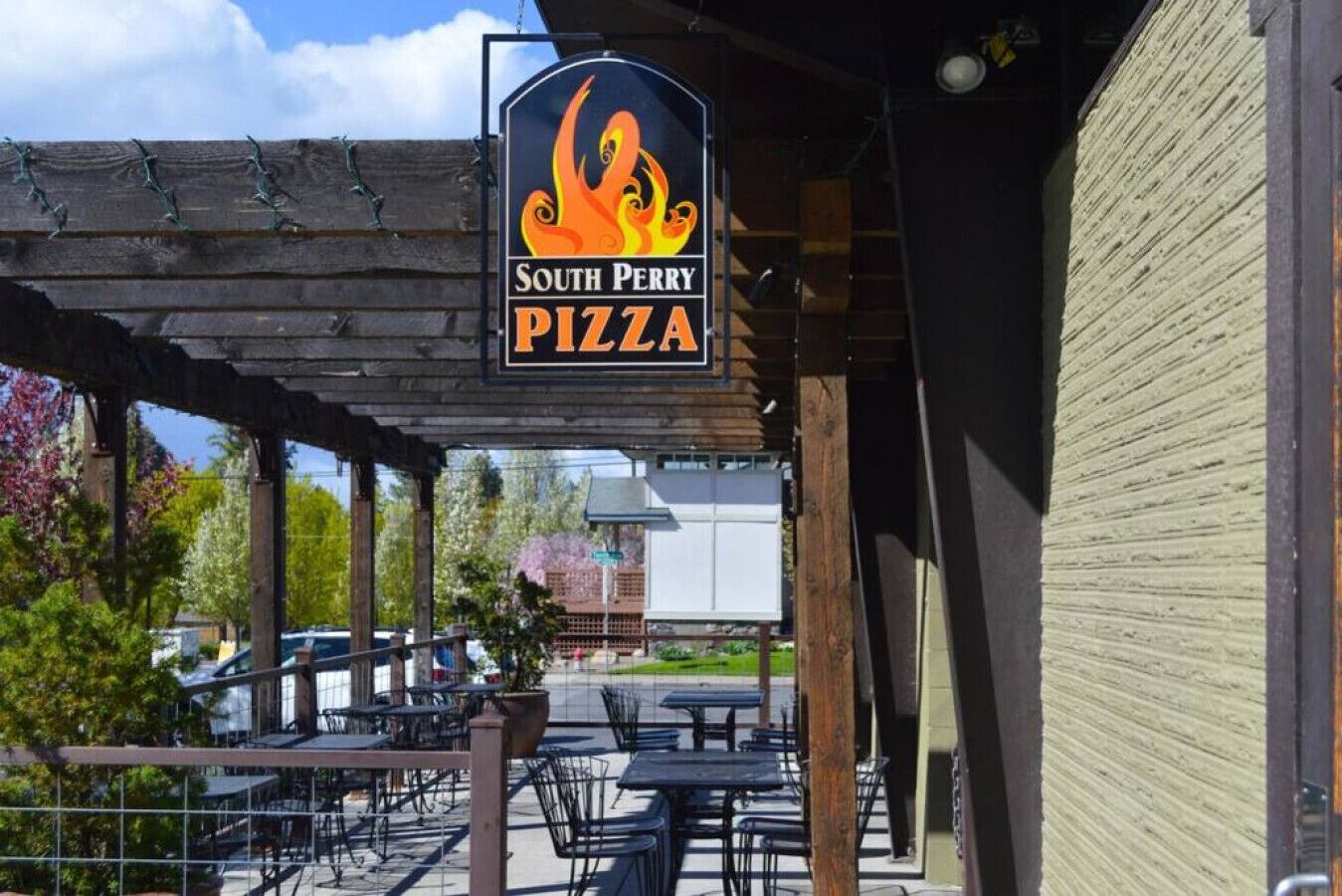 An outdoor seating area with tables and chairs, a wooden pergola, and a sign for South Perry Pizza.