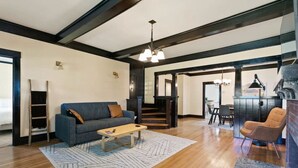 A spacious living room with a wooden floor, a blue sofa, a coffee table, and a staircase leading to another level. - Quaint South Hill Home w/ Luxury King Bed & Wifi! (Spokane)
