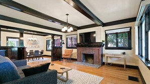 A spacious living room with a fireplace, a dining area, and large windows. - Quaint South Hill Home w/ Luxury King Bed & Wifi! (Spokane)