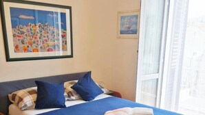 A bedroom with a bed, a window, and a painting on the wall.