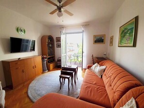 Una sala de estar con sofá, televisor, aparador de madera y ventilador de techo.