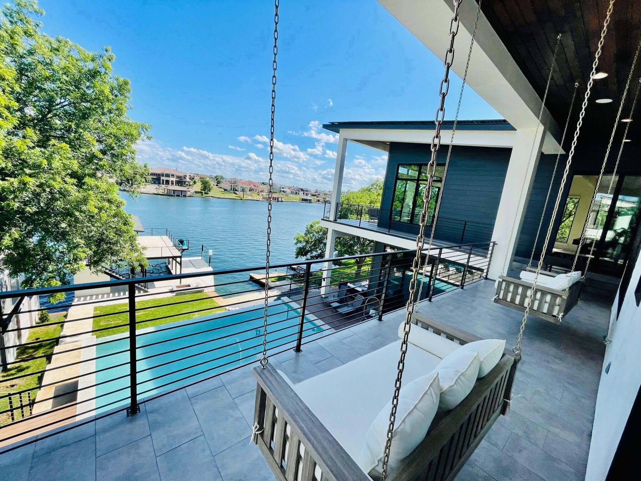 Un balcon doté d’une chaise suspendue donnant sur une piscine et un lac.