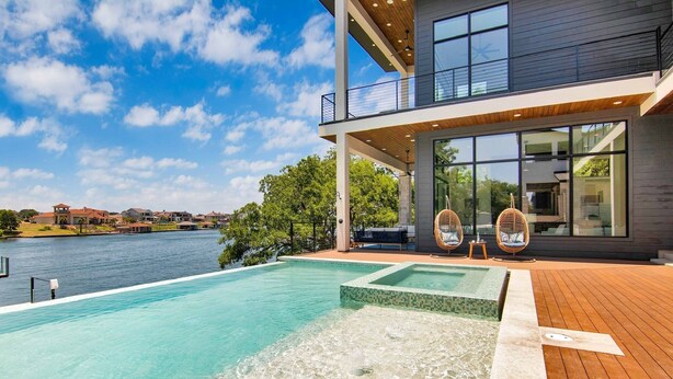 Una casa moderna con una piscina grande, terraza de madera y vista al agua.