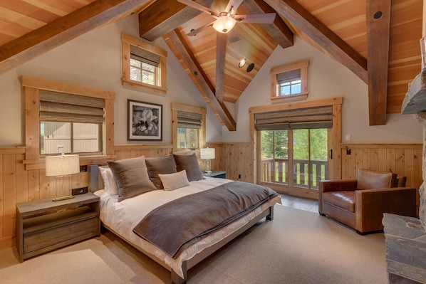 A spacious bedroom with a large bed, wooden ceiling beams, and multiple windows providing natural light.
