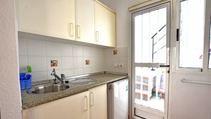 A small kitchen with white cabinets, a sink, and a refrigerator. - Beautiful, cozy vacation home on the Costa Calida, Andalusia 5 min. to the beach (San Juan de los Terreros Andalucia)