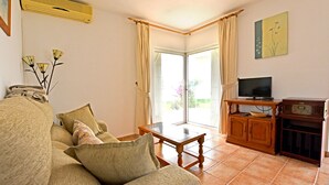 A living room with a sofa, a coffee table, a television, and a cabinet. There is a sliding glass door leading to a balcony. - Beautiful, cozy vacation home on the Costa Calida, Andalusia 5 min. to the beach (San Juan de los Terreros Andalucia)