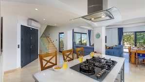 A modern kitchen with a central island, a dining area with blue sofas, and a staircase leading to an upper level. - Luxury Villa in Kisla, Kalkan Within Walking Distance to the Beach (Kalkan)