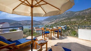 A terrace with a view of the sea and mountains, featuring a table, chairs, and a sun umbrella. - Luxury Villa in Kisla, Kalkan Within Walking Distance to the Beach (Kalkan)