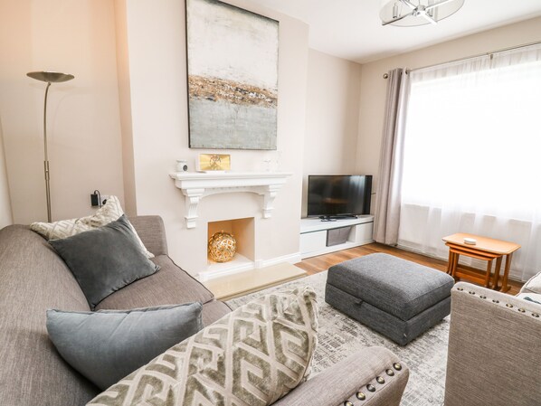 Una sala de estar con sofá, reposapiés, televisor, chimenea y una lámpara de pie.