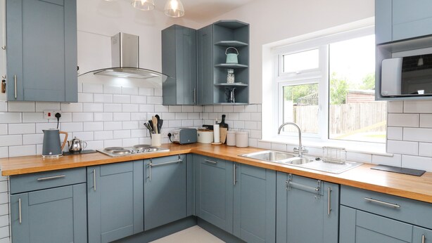 A modern kitchen with blue cabinets, a wooden countertop, a built-in stove, and a window providing natural light. - Welsh Valley House (Ammanford)