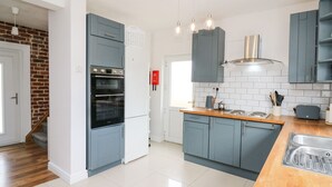 A modern kitchen with blue cabinets, a stainless steel range hood, and a wooden countertop. - Welsh Valley House (Ammanford)