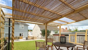 A covered patio area with a wooden table and chairs, a grill, and a view of the neighborhood. - Welsh Valley House (Ammanford)
