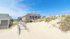 Una casa sulla spiaggia con veranda in legno, una scala che conduce all'ingresso e una spiaggia sabbiosa sullo sfondo.