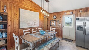 Una cucina con rivestimenti in legno, un tavolo da pranzo, sedie, un frigorifero e un orologio appeso al muro.