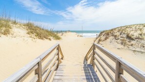Una passerella di legno che conduce a una spiaggia sabbiosa, con dune e l'oceano sullo sfondo.