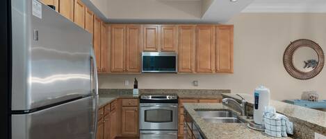 A modern kitchen with wooden cabinets, stainless steel appliances, granite countertops, and a microwave above the stove.