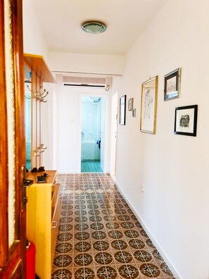 Enter a hallway with patterned floor tiles, leading to a bathroom with a wooden door and framed pictures on the walls.