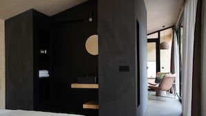 Quarto de hotel moderno com uma cama grande, um guarda-roupa escuro, uma prateleira de madeira e vista para a varanda.