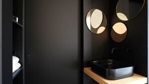 Uma casa de banho moderna com lavatório preto, estantes de madeira e três espelhos redondos.