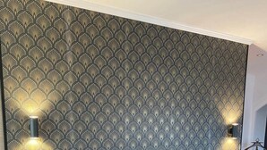 A bedroom with a patterned wallpaper, a wooden headboard, a nightstand with a plant, and two wall-mounted lights. - Rose Room (Saint-Didier-de-la-Tour)