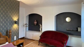 A room with a bed, a red armchair, a decorative wall with a patterned wallpaper, a vase, and a statue. - Rose Room (Saint-Didier-de-la-Tour)