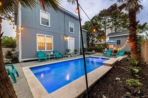 A residential backyard with a swimming pool, outdoor seating, and string lights.