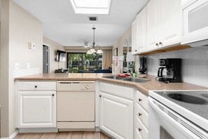 A modern kitchen with white cabinetry, a dishwasher, a stove, and a coffee maker. - Stunning Second Floor Park Shore Resort Unit 223 (Naples)