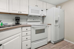 Une cuisine avec des meubles blancs, une cuisinière, un four à micro-ondes et un réfrigérateur.
