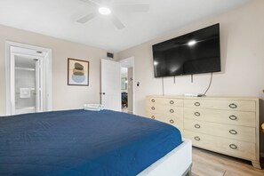 A bedroom with a bed, a dresser, a television, and a door leading to a bathroom. - Stunning Second Floor Park Shore Resort Unit 223 (Naples)