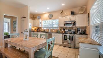 A modern kitchen with white cabinets, stainless steel appliances, and a wooden dining table.