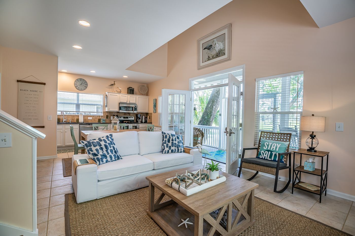 A spacious living room with a white sofa, a coffee table, and a dining area with a kitchen in the background.