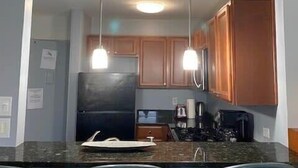 A compact kitchen with a central island, two pendant lights, wooden cabinets, and a black refrigerator. - Heart of ATL Downtown  1B1B  City View  Cozy Condo (Atlanta)