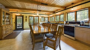 A spacious kitchen with wooden cabinets, a dining table, and large windows. - Spacious UP Retreat with Sauna & Direct Trail Access (Wetmore)