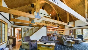A spacious living area with high ceilings and exposed wooden beams, furnished with leather sofas and a coffee table. - Spacious UP Retreat with Sauna & Direct Trail Access (Wetmore)