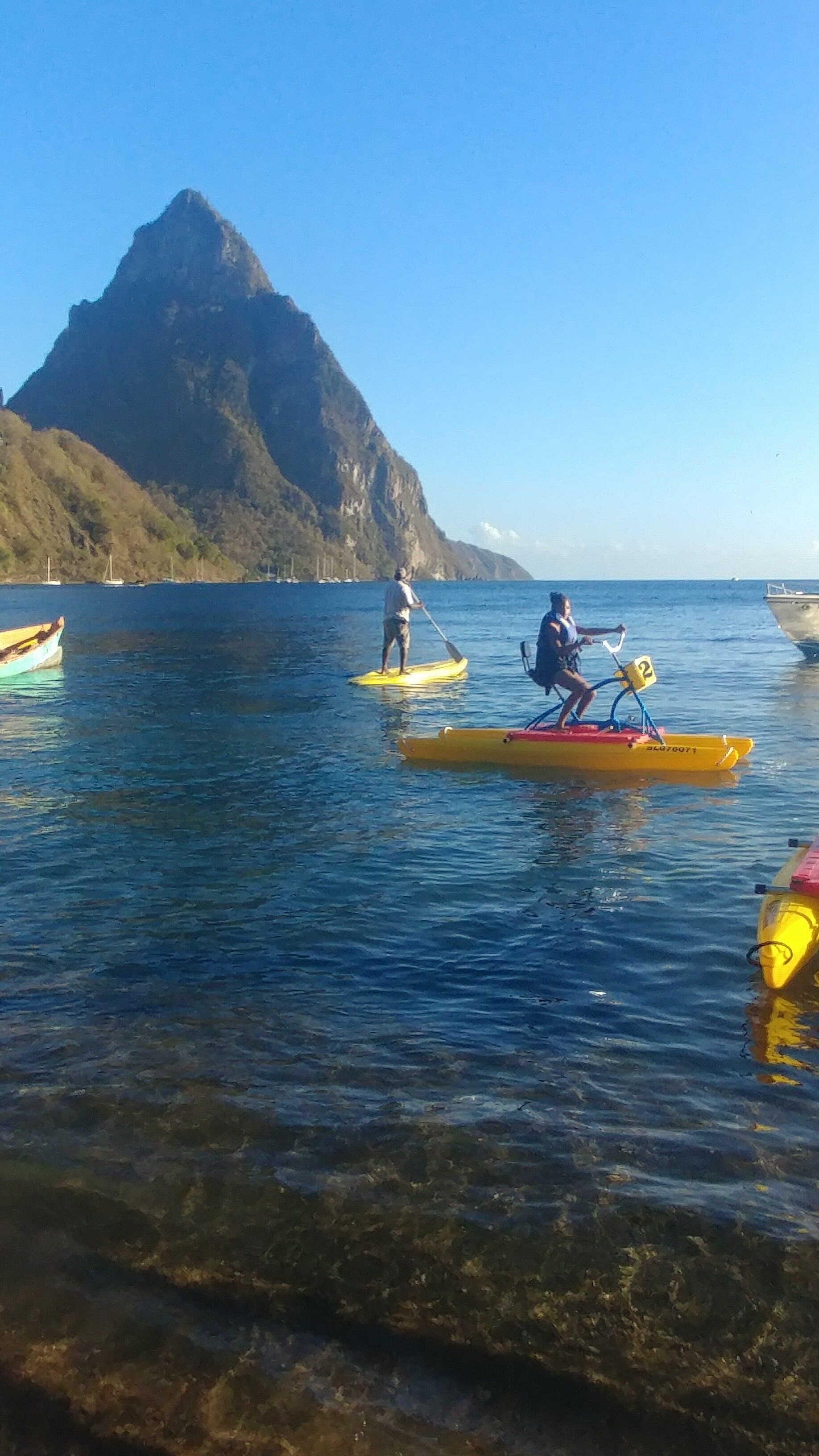 A calm body of water with kayaks and a mountain in the background.