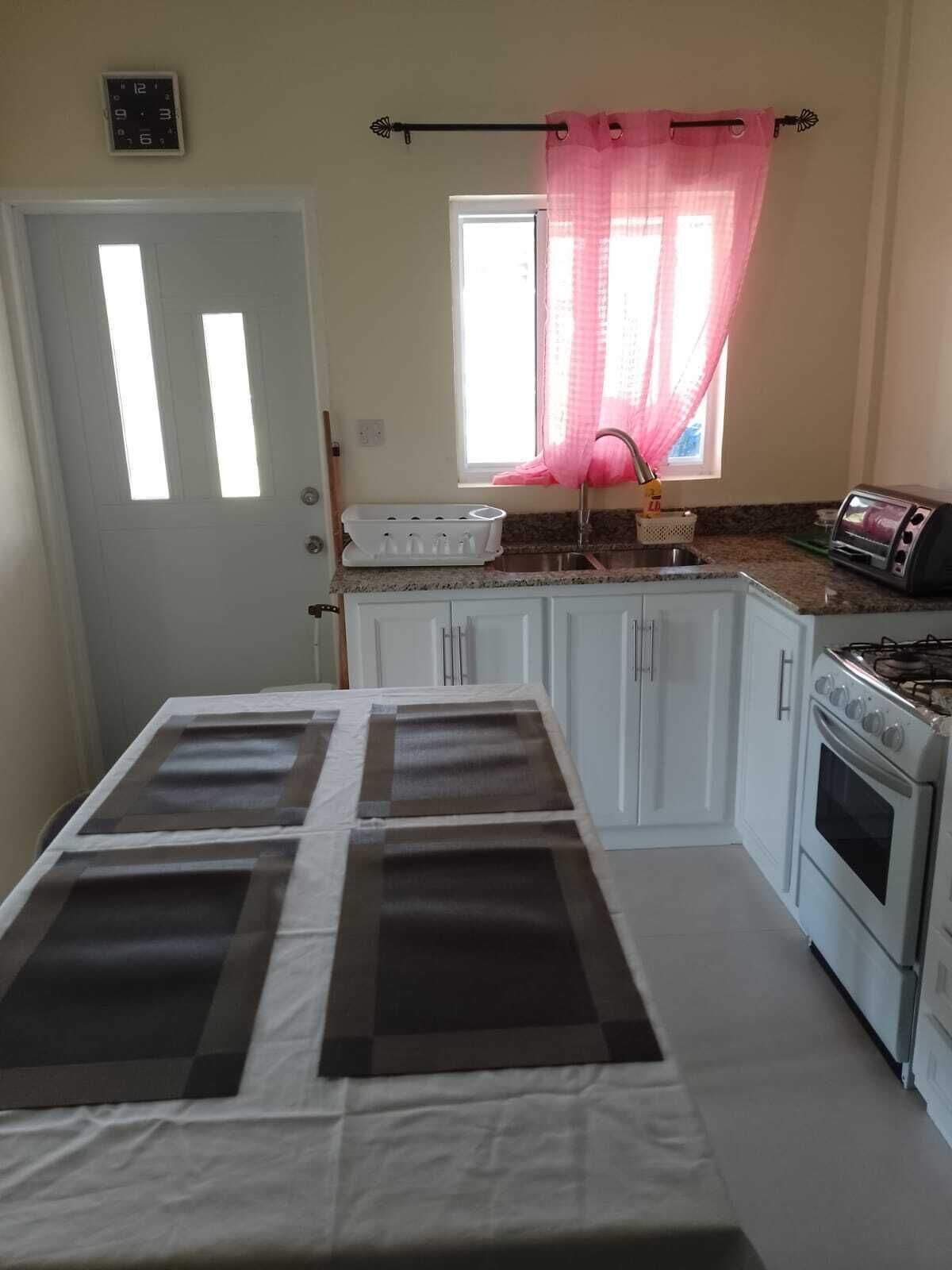 A compact kitchen with white cabinets, a gas stove, a toaster, and a window with pink curtains.