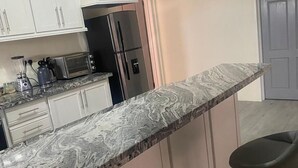 Una cocina con armarios blancos, encimera de mármol, refrigerador negro y un taburete de bar.