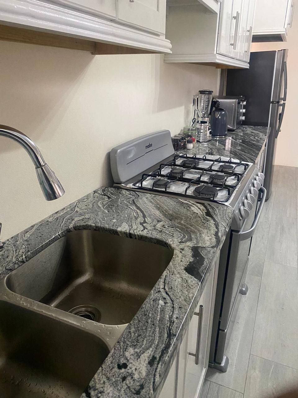 Een keuken met een granieten aanrecht, een roestvrijstalen spoelbak en een gasfornuis.