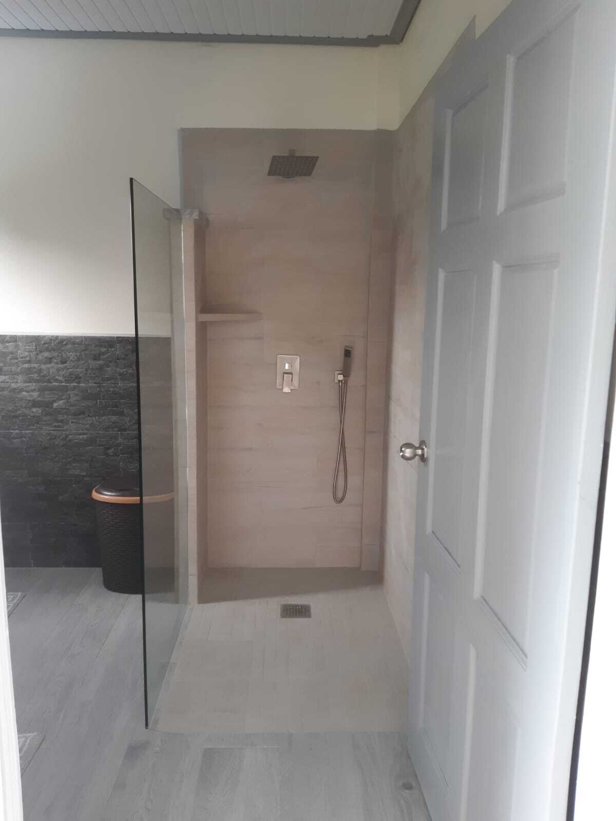 Una ducha a ras de suelo con puerta de vidrio, suelo de madera y pared de acento de piedra.