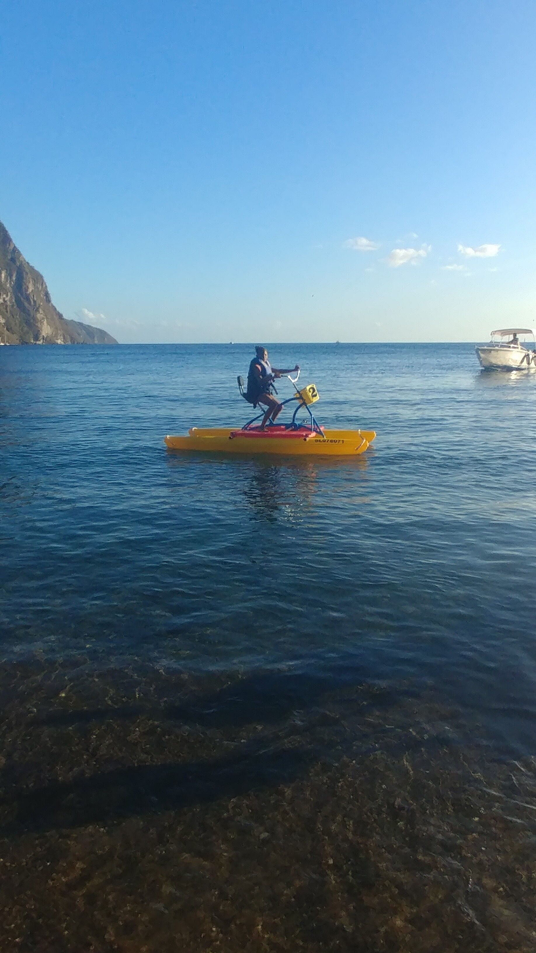 A person paddling a yellow kayak on calm water with a clear sky and a distant boat.