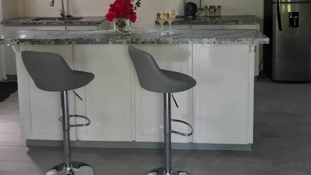 Una cocina moderna con armarios blancos, un refrigerador de acero inoxidable, dos taburetes de bar y luces colgantes.