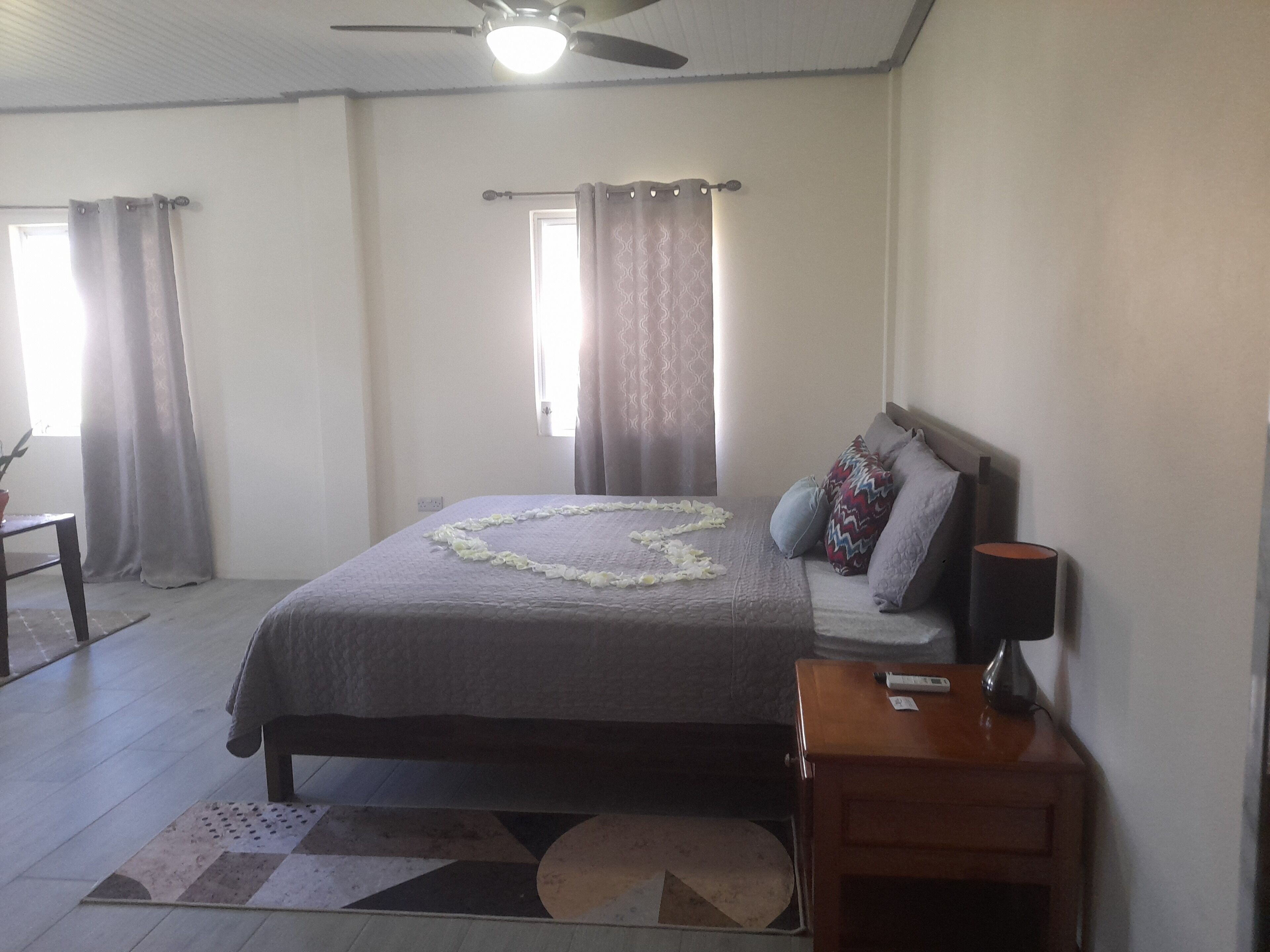 A bedroom with a bed, a nightstand, a ceiling fan, and a window with curtains.