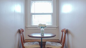 Une pièce d’angle avec une fenêtre, une table ronde ornée d’un vase de fleurs, deux fauteuils rembourrés et un banc en bois.