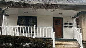 Une maison à deux étages avec un porche à l’avant, une porte en bois et une boîte aux lettres.