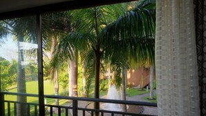 A view from a balcony with a fountain, palm trees, and a building in the background. - Hilltop condo with beautiful ocean view! (Tarcoles)