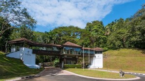 A modern building with a covered entrance, surrounded by lush greenery and a clear sky. - Hilltop condo with beautiful ocean view! (Tarcoles)