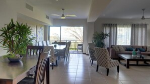 A spacious living area with a dining table, chairs, a sofa, and a balcony with large windows. - Hilltop condo with beautiful ocean view! (Tarcoles)