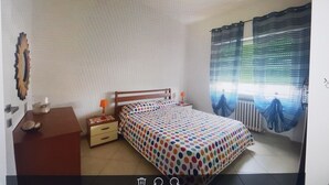 A bedroom with a bed, a nightstand, a dresser, a window with curtains, and a radiator. - TWO-ROOM APARTMENT PIOMBINO MARE 50 MT - 4 PANORAMIC BEDS (Piombino)