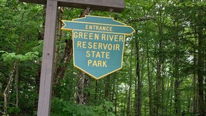 A wooden sign indicating the entrance to Green River Reservoir State Park with a notice that all visitors must pay a fee. - Cozy 3 bedroom 2 bath home close to hiking, biking, and Stowe! (Hyde Park)
